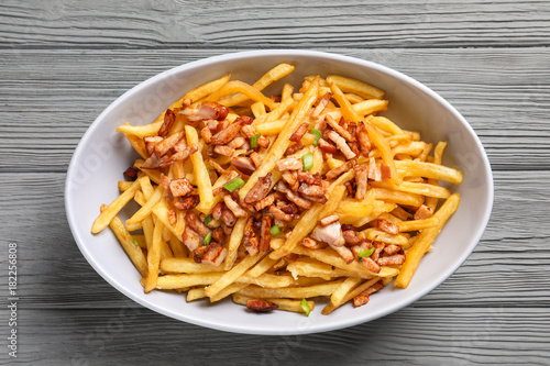 Plate with french fries and bacon on wooden background
