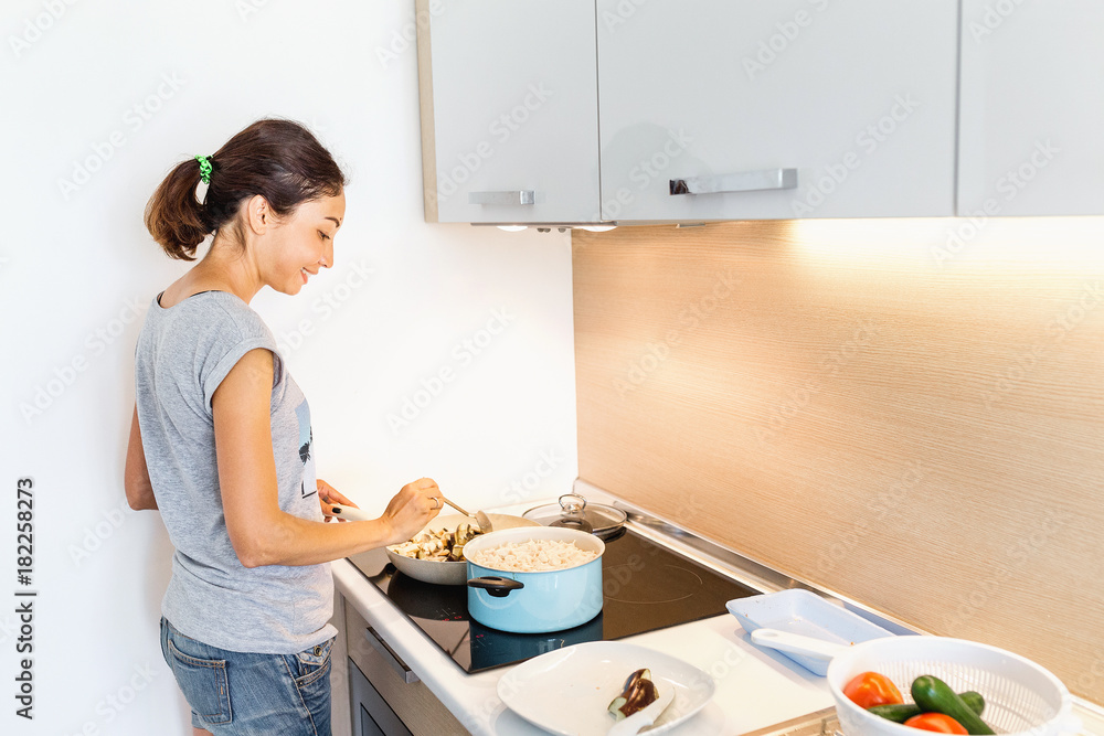 Φωτογραφία A woman housewife in the kitchen prepares food in a special ferromagnetic dish on an induction cooker