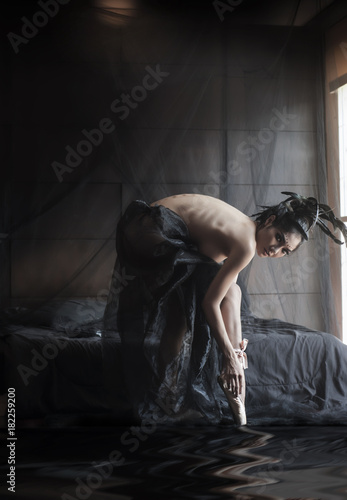 Asian ballerina woman in black swan top nude concept costume wearing pink ballet shoes in the dark bed room natural window light with digital reflection effect.