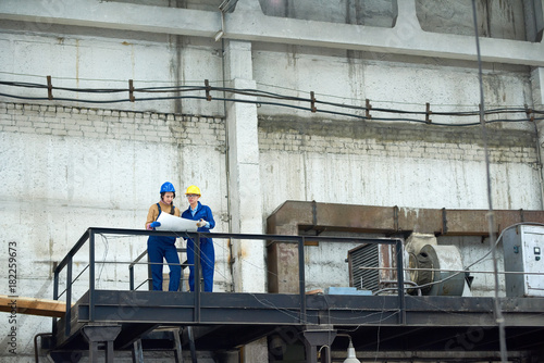 Foto Busy confident female factory workers analyzing blueprint while working in old f