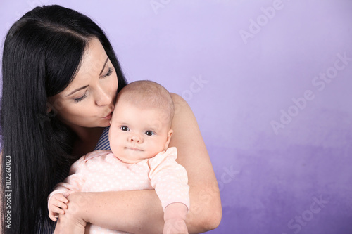 Young mother and cute baby on color background