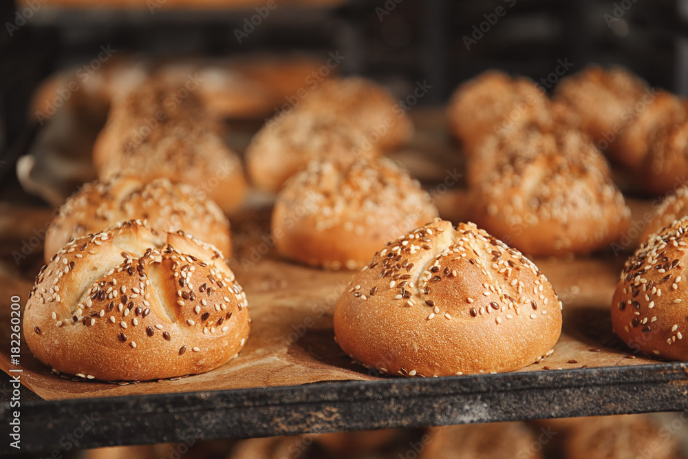 Tasty buns with sesame on baking tray, closeup