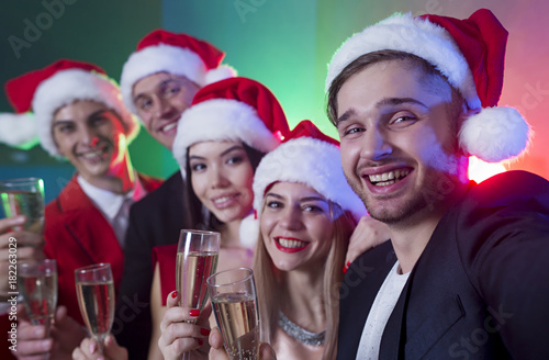 Group of smiling friends in Santa hats are photographed or make selfie on New Year's party