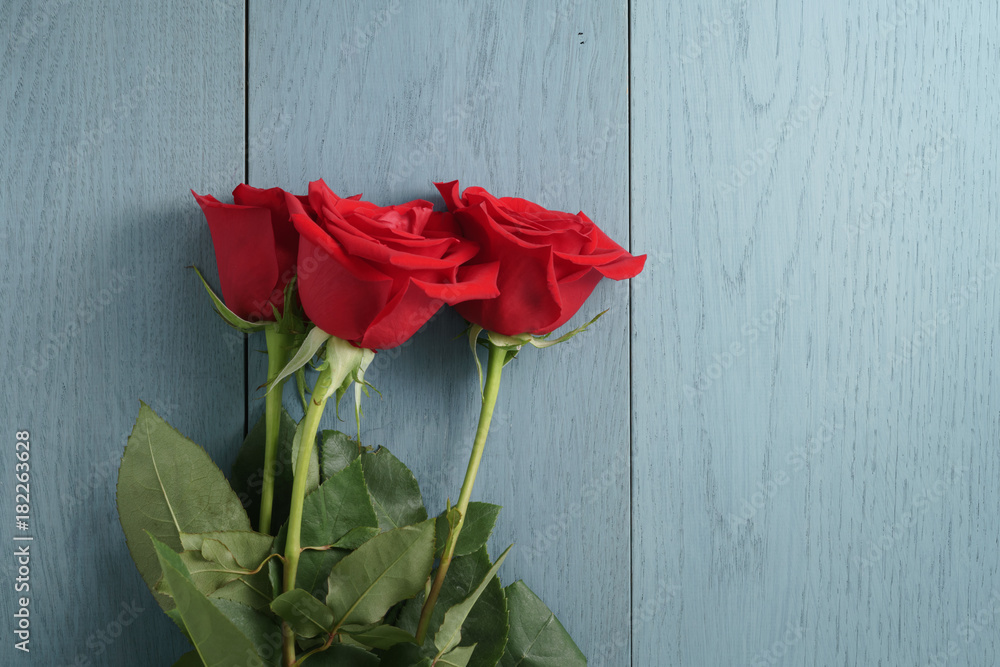 three red roses on blue wood table with copy space