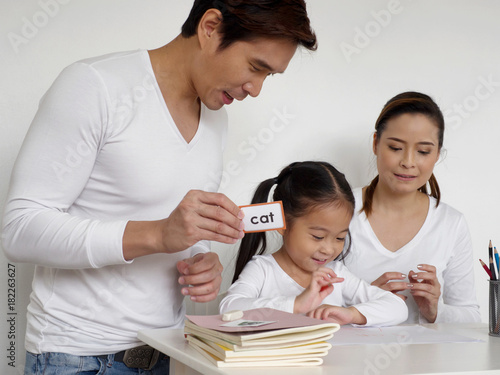 asian kid learning english with her father and mother at home