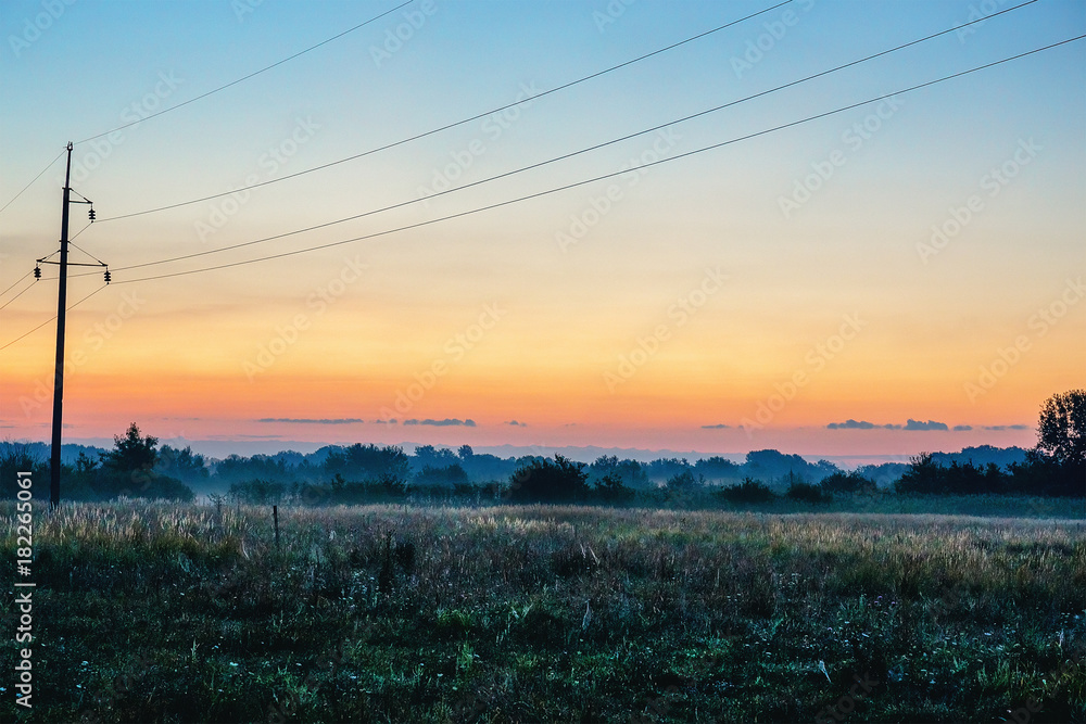 Power lines in misty sunrise over firld