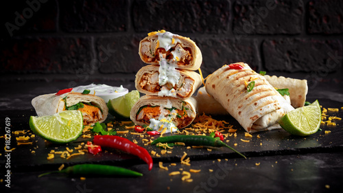 Healthy grilled chicken and parsley wraps, loaded with cheese, served with greek yogurt deep, chillies and lime slices photo