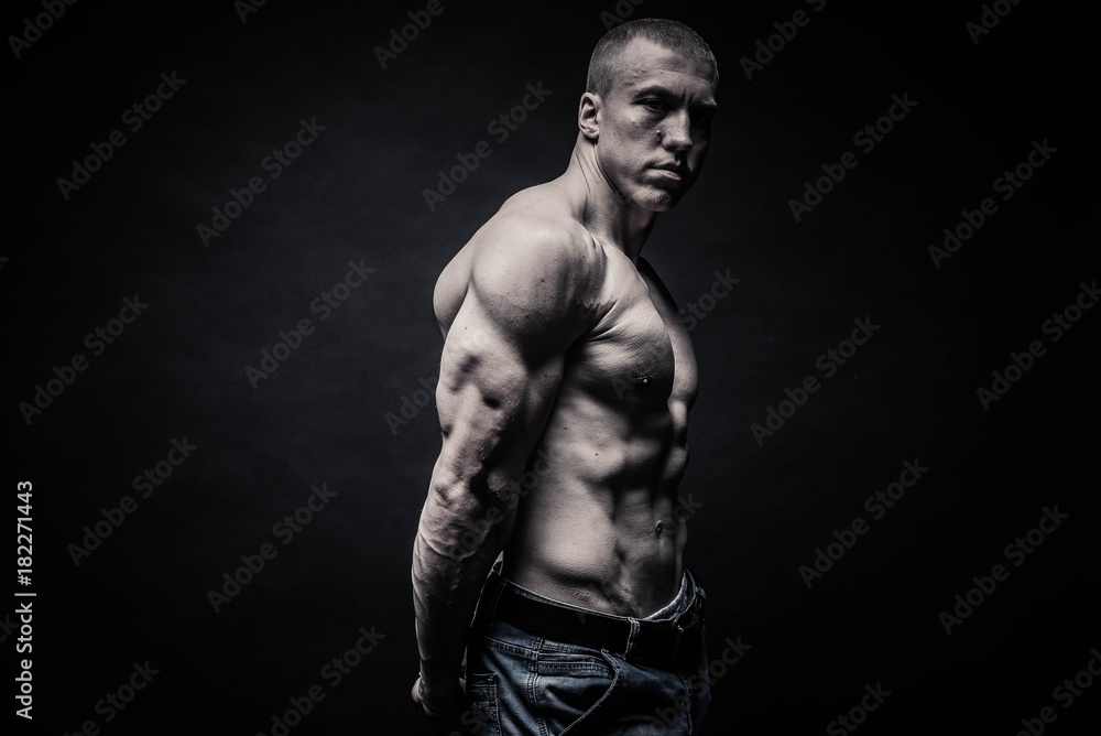 Naklejka premium portrait of a male bodybuilder, straining muscles in sports poses, on a black background is isolated. monochrome. The concept of a photo of competing sports, health, fitness