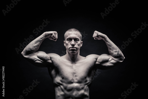 portrait of a male bodybuilder, straining muscles in sports poses, on a black background is isolated. monochrome. The concept of a photo of competing sports, health, fitness