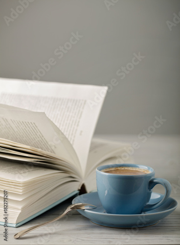 Coffee in a light blue cup and book in blue cover on a wooden background.