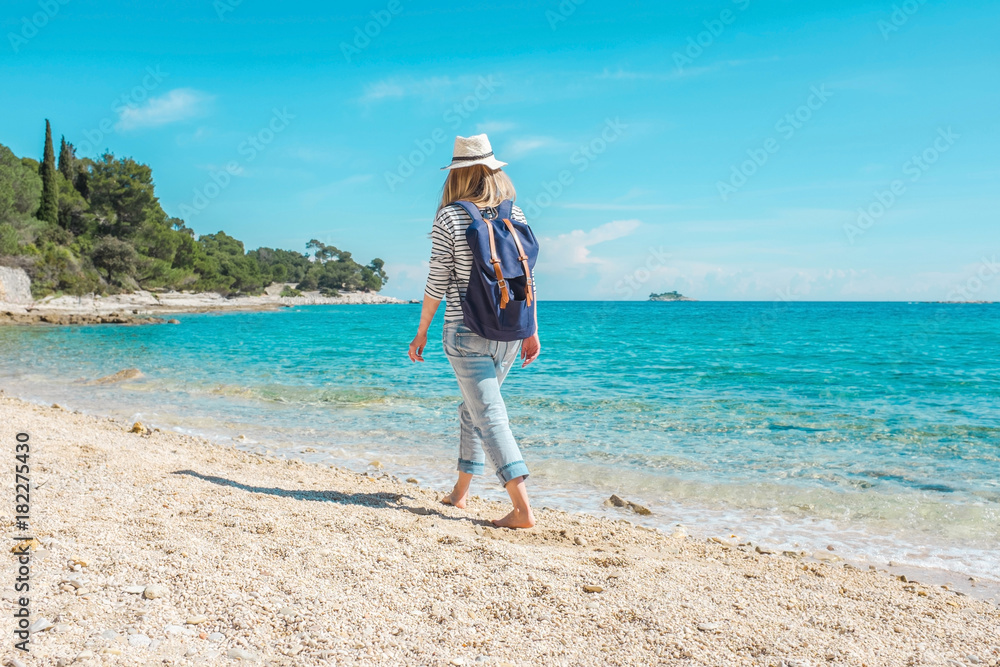 Blonde woman in summer hat with her backpack walking in the sand Blonde woman in summer hat with her backpack walking in the sand
