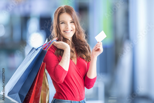 Beautiful happy girl with credit card and shopping bags in shopping mall. Shopping Center in the background.