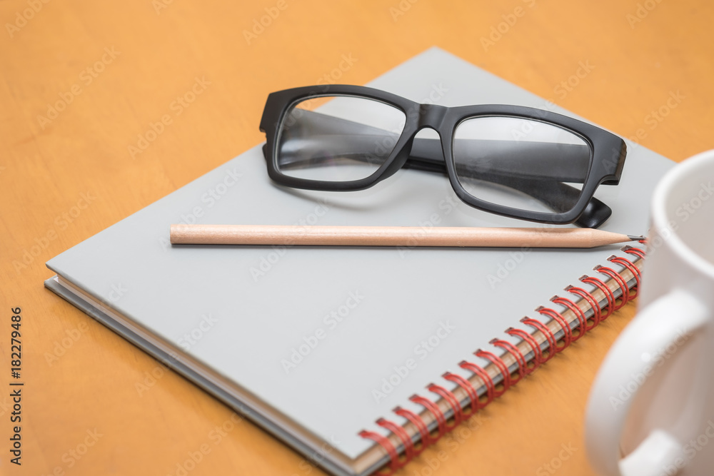 Work and education concept. Reading glasses, pencil, notebook and cup of hot coffee on wooden table. Work and education concept. Reading glasses, pencil, notebook and cup of hot coffee on wooden table.