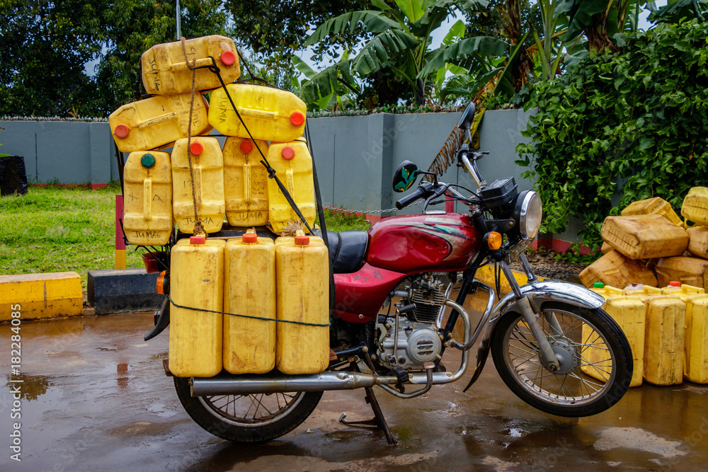 Fototapeta premium A typical boda boda, motorbike, in Uganda transporting many water canisters at once. The motorbike is parking at a gas station near Mbale.