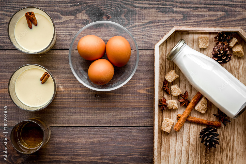 Make eggnog classic recipe. Eggs, milk, cinnamon, whiskey on dark wooden background top view Make eggnog classic recipe. Eggs, milk, cinnamon, whiskey on dark wooden background top view