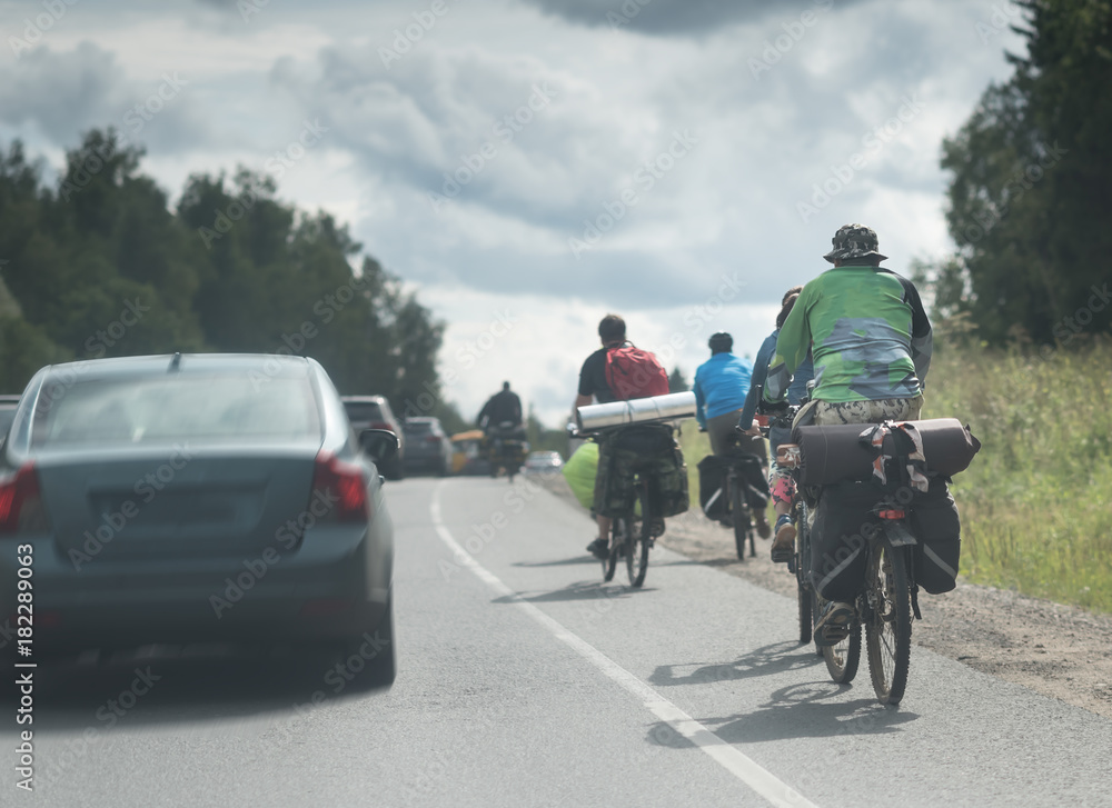 group of tourists with backpack travels with bicycle outdoors on the asphalt road