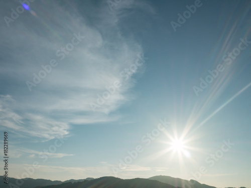 blue cloudy sky background with the sun and silhouette mountain