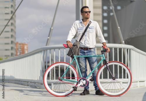 Fototapeta Naklejka Na Ścianę i Meble -  A young stylish man with sunglasses posing next to his bicycle.