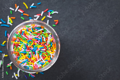 Tablou pe pânză Colorful sugar sprinkles in glass jar, photographed overhead on slate (Selective