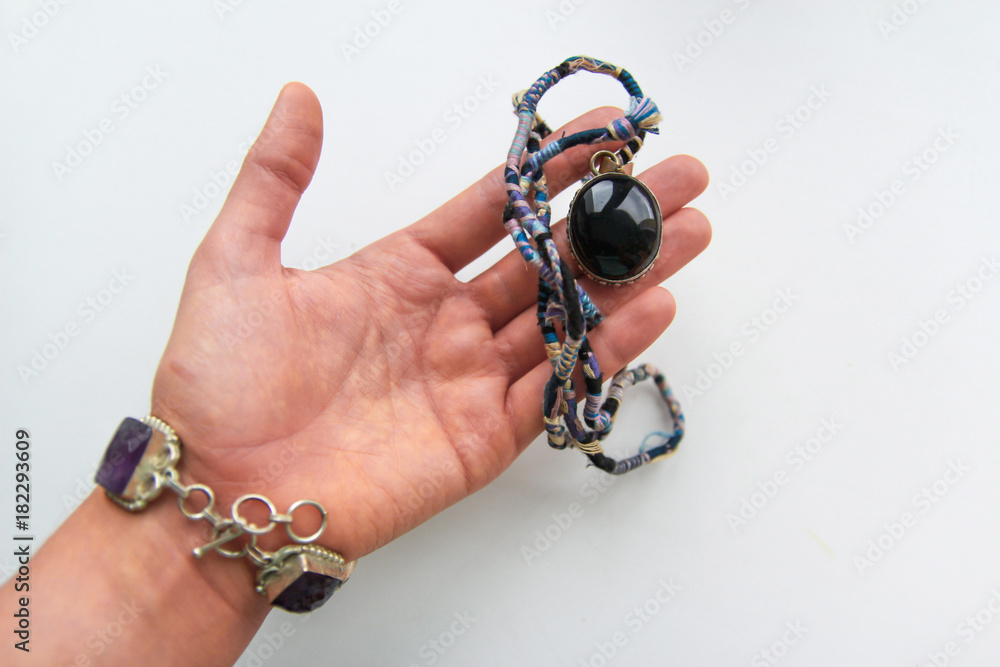 Female hand in a silver bracelet with large stones of blue and gray colors holding a black pendant on a white background Female hand in a silver bracelet with large stones of blue and gray colors holding a black pendant on a white background