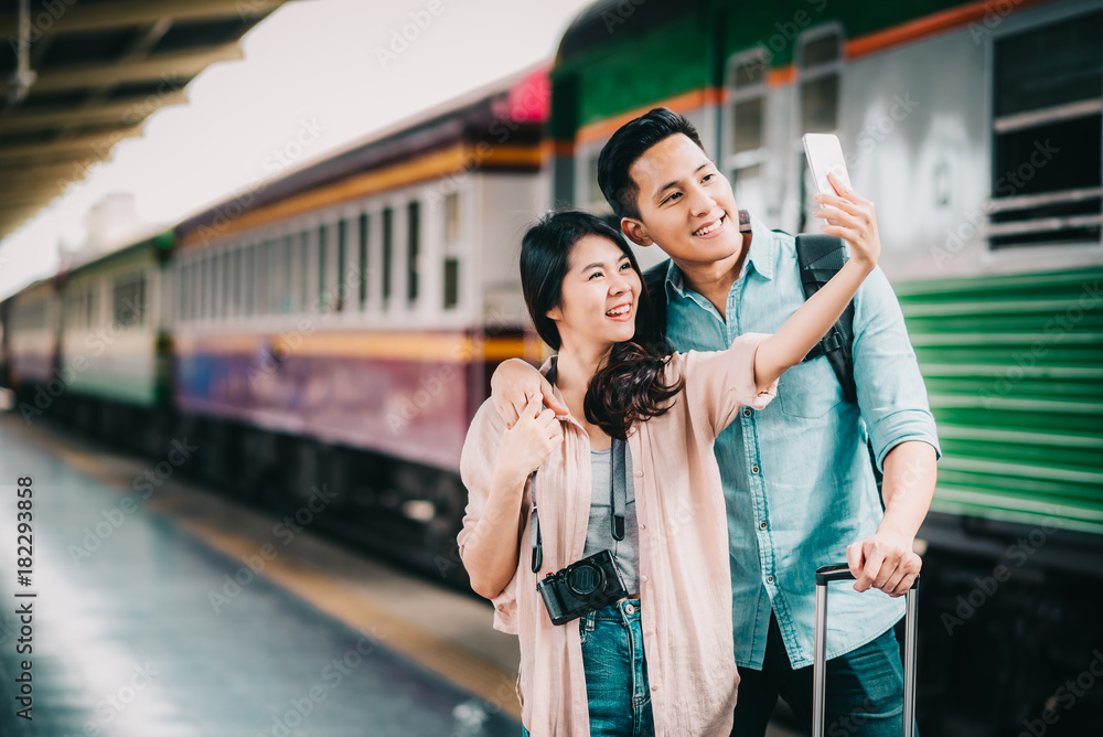 Happy Asian traveler couple taking selfie with smartphone at train station during vacation trip