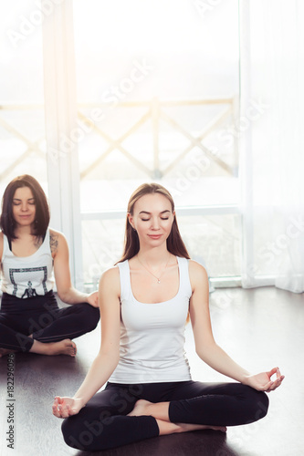 Yoga group concept. Young couple meditating together, sitting back to back on windows background, copy space