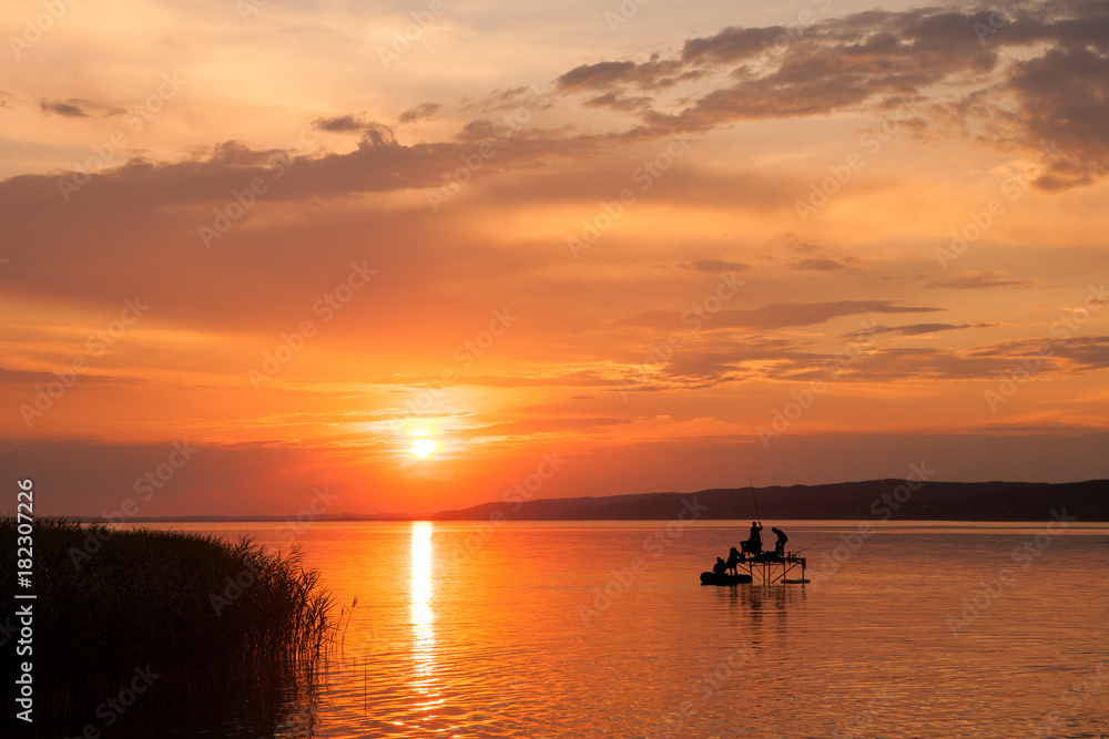 Beautiful sunset over Lake Balaton with silhouettes of anglers an reed