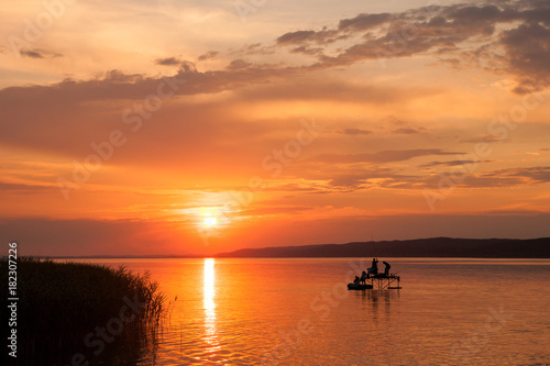 Beautiful sunset over Lake Balaton with silhouettes of anglers an reed © andras_csontos