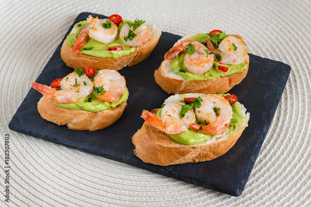 Bruschetta italian snack sandwiches with avocado cream and prawns decorated by parsley and chilli peppers.