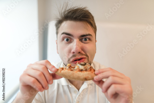 Portrait of hungry man with a piece of pizza in his hands. The man eats a pizza and looks at the camera. Fast food lunch.