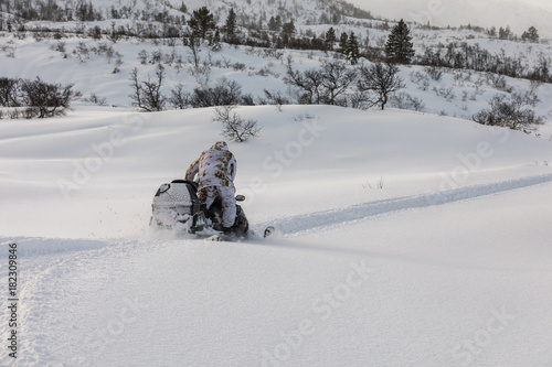 Man driving snowmobile in the snow, seen from behind