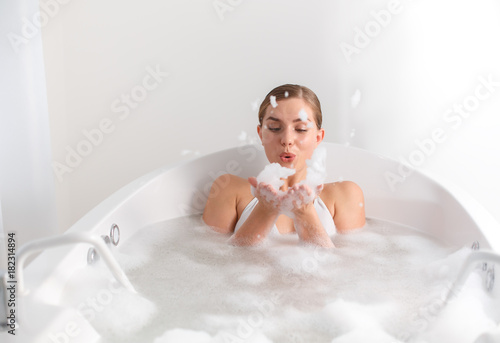 Joyful girl is playing with foam while taking a bath at spa photo