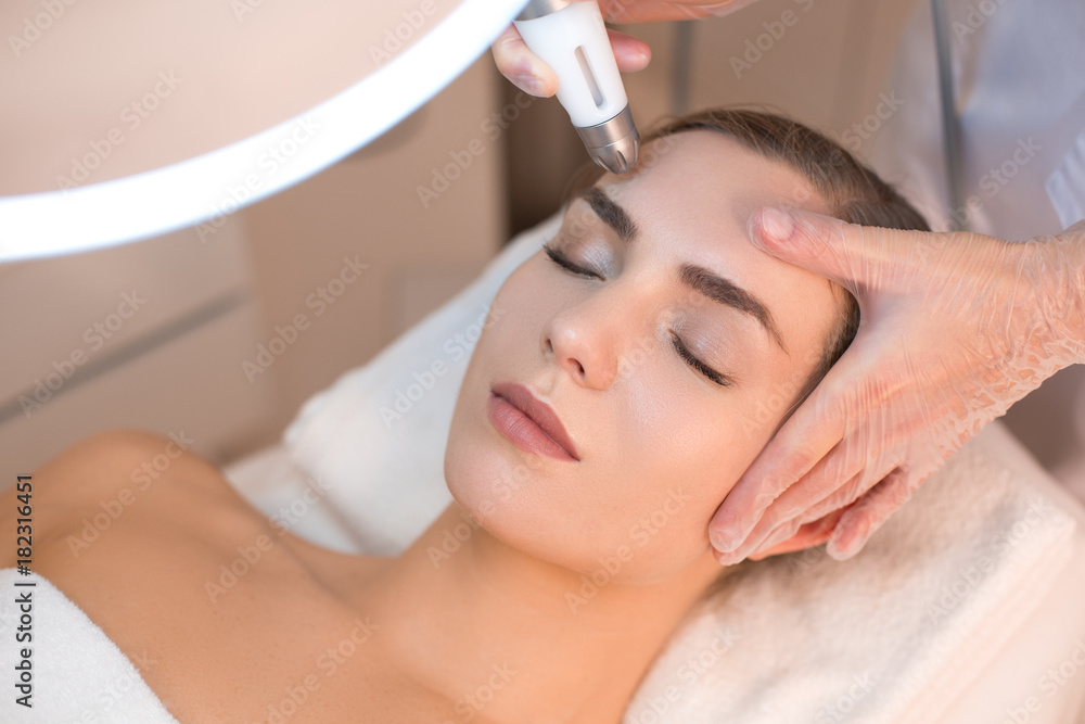 Close up of female face having laser rejuvenating treatment. Cosmetologist hand lifting equipment over her forehead. Beauty concept