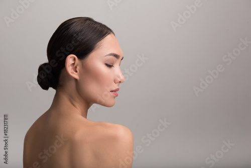 Skincare and beauty concept. Profile of charming serious young asian girl is looking down thoughtfully while demonstrating her perfect and fresh skin. Isolated background with copy space in right side