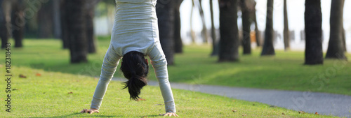 Fototapeta Young woman practice handstand on park meadow