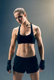 What are you waiting for. Muscular young sportswoman wearing boxing wraps showing her well trained body while posing for the camera over a dark background.