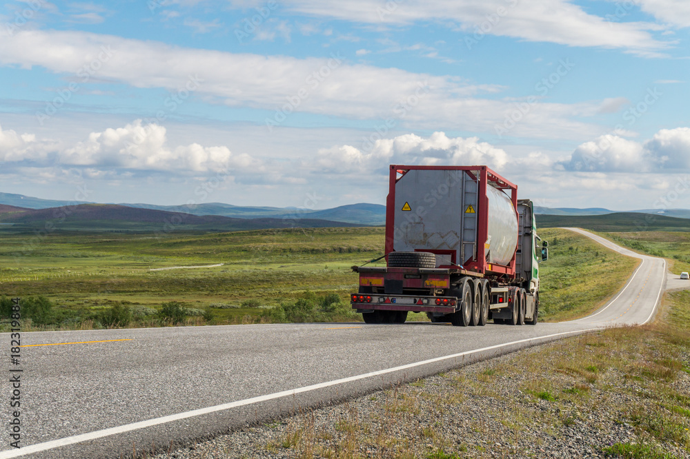 Large tanker truck on the road on a background of a green meadow and clouds