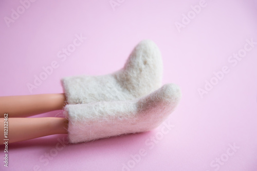 woolen warm winter shoes valenki on the doll feet on a pink background. the concept of winter. winter shoes