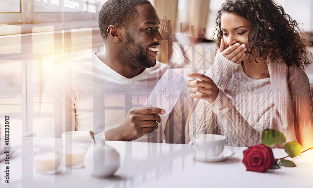 Planning future travel. Close up of young positive man showing flight tickets while his girlfriend covering her face and expressing surprise Planning future travel. Close up of young positive man showing flight tickets while his girlfriend covering her face and expressing surprise
