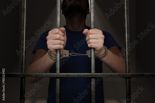 Arrested prisoner is holding bars in prison cell. photo