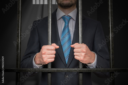 Businessman or politician behind bars in prison cell.