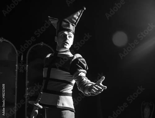Actor dressed jester's costume in interior of old theater. Black-white portrait.