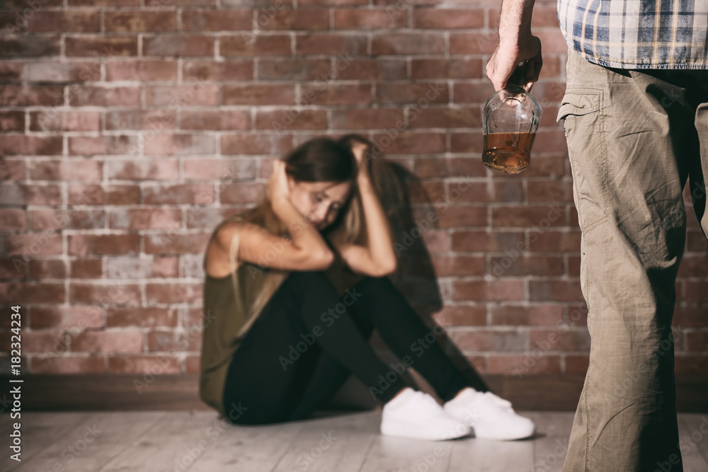Man with bottle of alcohol and young woman against brick wall