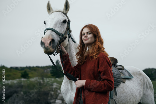 Young beautiful woman in the mountains walking with a white horse