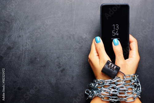 Woman hands tied with metallic chain with padlock on dark background suggesting internet or social media addiction photo