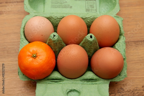 Satsuma, or small orange, in an egg carton, alone with five eggs. Odd one out concept.
