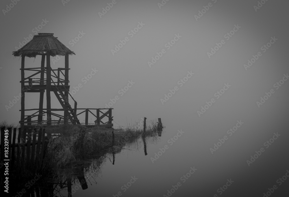 a wooden tower standing on the bank of a foggy autumn river on a cloudy, sad day