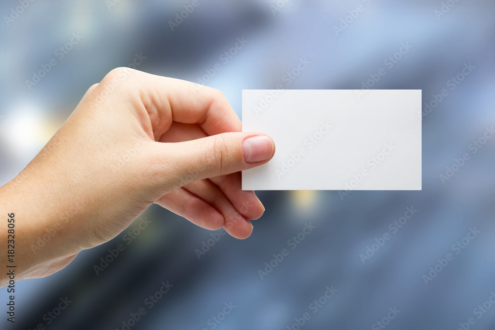 Hands holding a white business visit id card, gift, ticket, pass, present showing close up on blurred blue background. Copy space for ad text Hands holding a white business visit id card, gift, ticket, pass, present showing close up on blurred blue background. Copy space for ad text