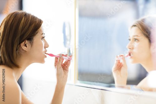young woman brushing teeth and looking in the mirror.