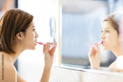 Obraz na plátně young woman brushing teeth and looking in the mirror.